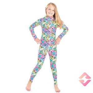 May include: A girl wearing a long-sleeved, one-piece outfit with a colorful, psychedelic print featuring peace signs, hearts, and other symbols. The outfit is made of a stretchy, comfortable fabric.