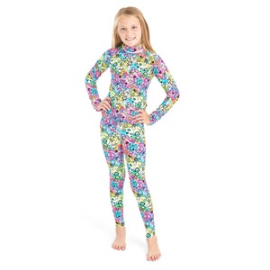 May include: A girl is wearing a long-sleeved, colorful, patterned top and matching leggings. The pattern features peace signs, hearts, and other symbols.