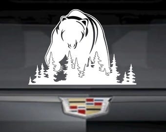 Könnte beinhalten: Weißer Vinyl-Aufkleber mit einem Bären, der durch einen Wald aus stilisierten Kiefern läuft. Der Bär steht im Mittelpunkt, mit detaillierten Linien, die seine Form definieren. Der Aufkleber ist für die Anbringung an der Heckscheibe eines Fahrzeugs oder einer ähnlichen Oberfläche konzipiert.