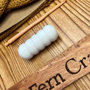 May include: A white, 3D printed, textured, round, crochet hook resting on a wooden ruler with the text "& Fern Craft" engraved on it.