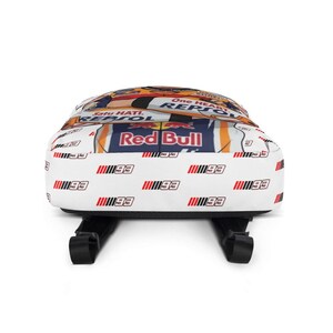 Puede incluir: Una mochila blanca con un patr&oacute;n repetitivo del n&uacute;mero 93 en negro y rojo. El panel superior muestra un gr&aacute;fico con el texto One Heart, Satu Hati, Repsol y logotipos de Red Bull en colores naranja, azul y blanco con correas negras.
