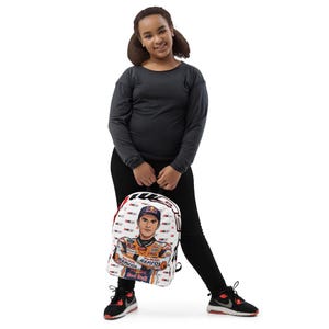 Puede incluir: Una mochila blanca con un patr&oacute;n repetitivo del logotipo de Repsol Honda y un gr&aacute;fico central de un piloto de motos con traje y gorra de Repsol. La mochila tiene bordes negros, un asa superior y correas ajustables para los hombros.