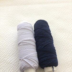 May include: Two spools of thread, one white and one navy blue.