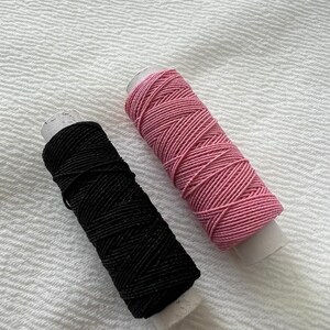 May include: Two spools of thread, one black and one pink, are wrapped around cardboard.