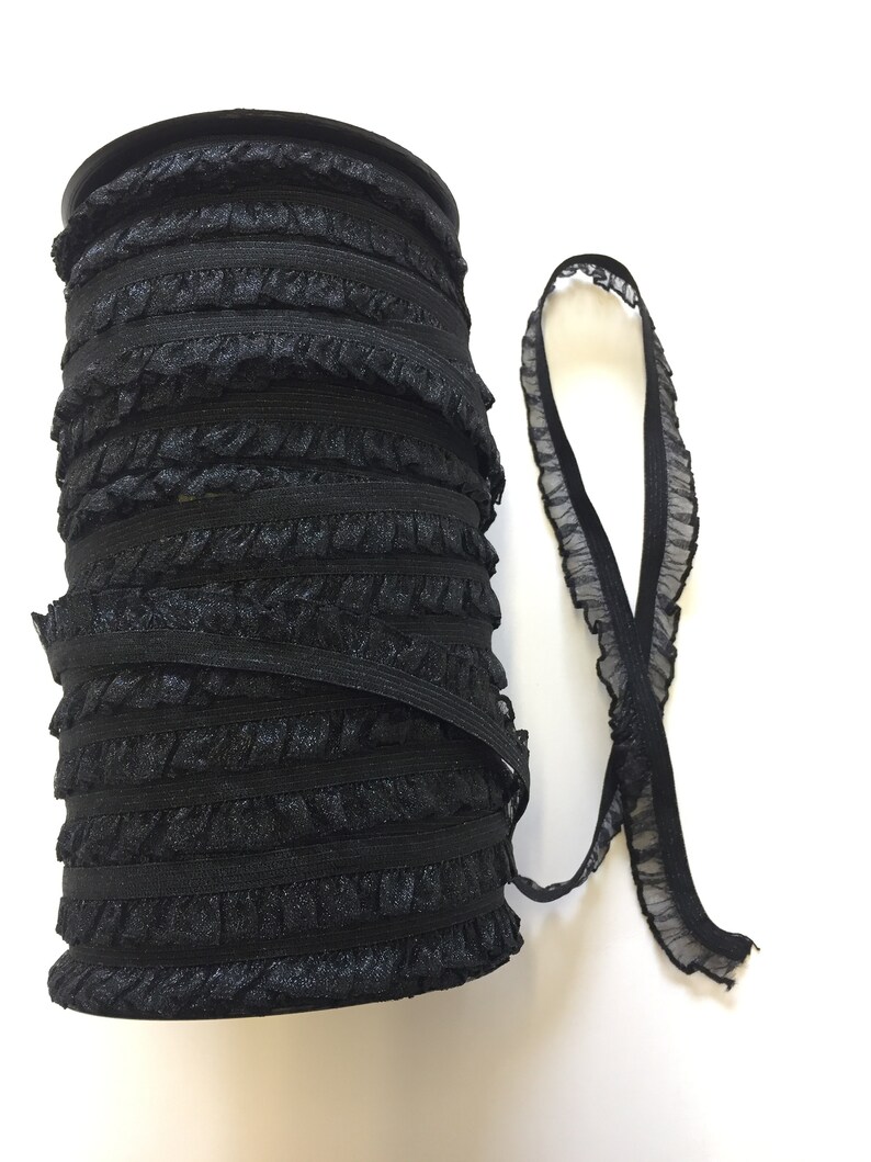 May include: A roll of black elastic trim with a ruffled edge. The trim is wound around a cardboard spool.