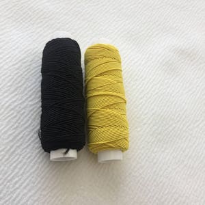 Op de afbeelding: Twee spoelen elastisch garen, een zwarte en een gele.