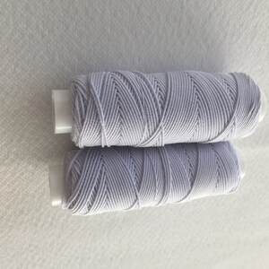 以下が含まれることがあります： 白いプラスチックのボビンに巻かれた、白い伸縮性のある糸の糸巻きが2つ