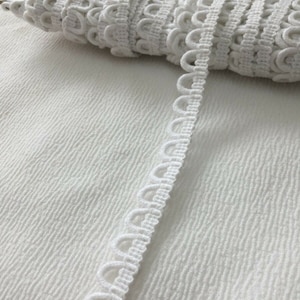 May include: White crocheted trim with a scalloped edge. The trim is made of a soft, delicate material and has a subtle sheen.