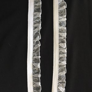 May include: Two white elastic trims with a ruffled tulle edge. The trims are against a black background.