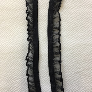 May include: Two black elastic trims with a ruffled edge. The trim is made of a sheer fabric with a subtle shimmer.