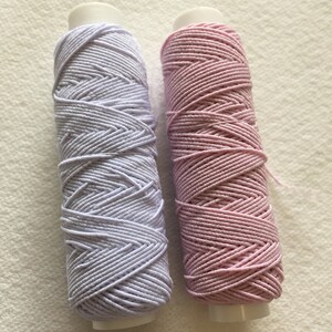 May include: Two spools of elastic thread, one lavender and one pink.