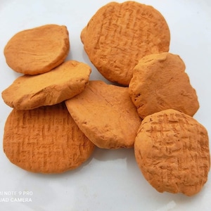 May include: A collection of seven round, orange clay discs with a textured surface. The discs are arranged in a pile on a white surface.