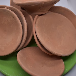 Può includere: Un set di sei ciotole in terracotta, tutte della stessa dimensione e forma, su un piatto verde. Le ciotole sono non smaltate e hanno un colore naturale terroso.