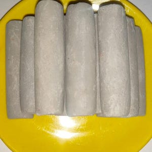 Puede incluir: Primer plano de varios objetos cilíndricos grises dispuestos sobre un plato amarillo brillante. Los cilindros, posiblemente de tiza, están colocados juntos. El plato amarillo vibrante contrasta con los cilindros grises.