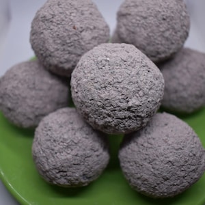 May include: A close-up of a pile of gray, round, textured treats on a green plate.