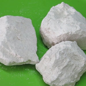 May include: Three white, irregularly shaped rocks on a green surface. The rocks have a rough, textured surface.