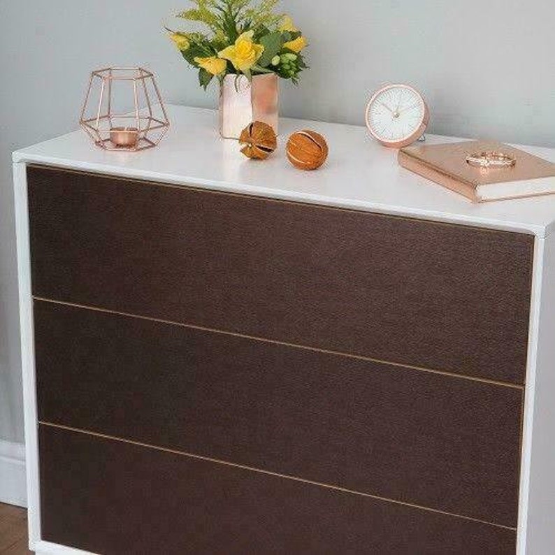 May include: A three-drawer chest of drawers with a white top and brown wood drawers. The chest has a modern design with clean lines and a simple aesthetic.
