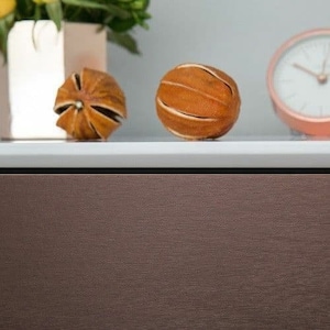 May include: Two dried orange peels, one with a starburst shape and the other round, sit on a white surface in front of a brown cabinet.