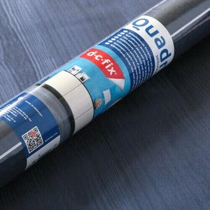 Puede incluir: Un rollo de película autoadhesiva de color azul oscuro con una etiqueta blanca y azul que dice "dc-fix Quadro Película Decorativa Autoadhesiva".