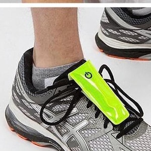 May include: A pair of grey running shoes with a bright green reflective strap attached to the laces. The strap has a power button icon on it.