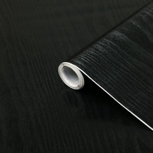K&ouml;nnte beinhalten: Eine Rolle schwarzes Holzdekor-Kontaktpapier. Das Papier hat eine dezente Holzmaserung und eine gl&auml;nzende Oberfl&auml;che.