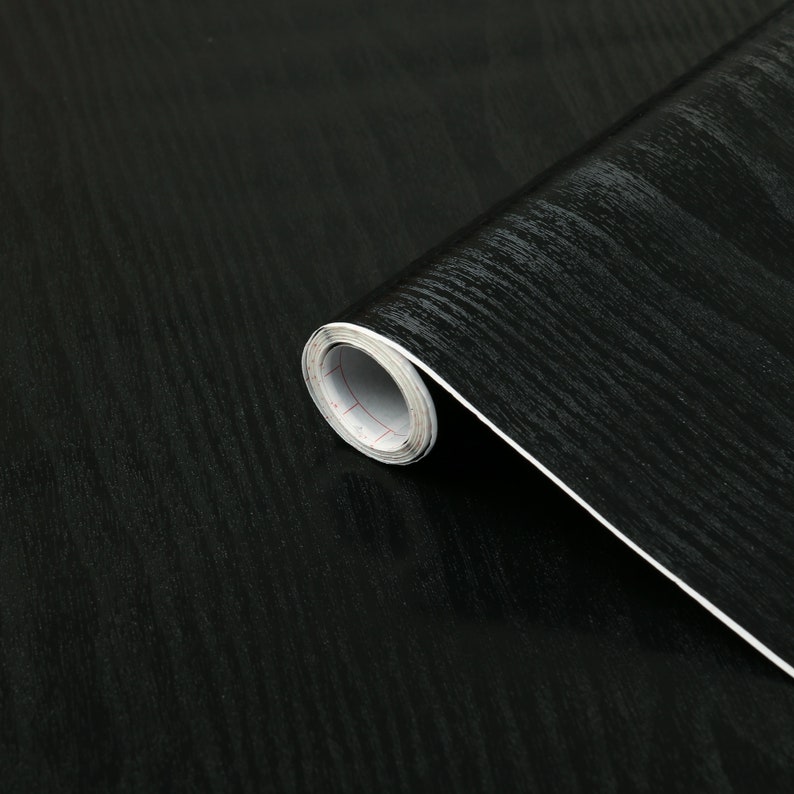 K&ouml;nnte beinhalten: Eine Rolle schwarzes Holzdekor-Kontaktpapier. Das Papier hat eine dezente Holzmaserung und eine gl&auml;nzende Oberfl&auml;che.