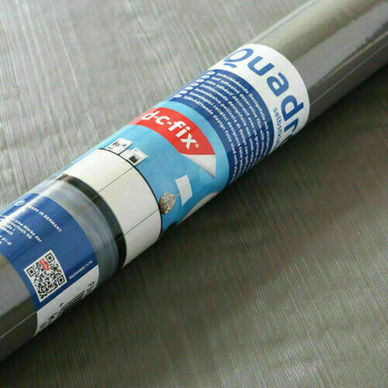 May include: Roll of gray self-adhesive contact paper with the text "quadrat selbstklebend" and "dc-fix" printed on the label. The label also includes a QR code and the text "Made in Germany".