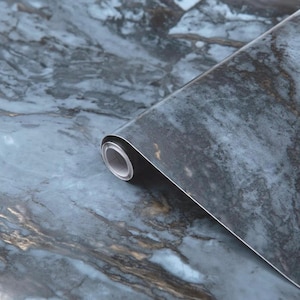 Pode incluir: Um rolo de papel de contacto de mármore azul e dourado. O papel tem um padrão de mármore realista com redemoinhos azuis claros e escuros e acentos dourados.