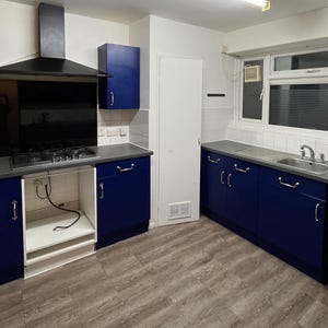 May include: A kitchen with blue cabinets, a black range hood, and a stainless steel washing machine. The kitchen has white tile backsplash and a gray countertop.