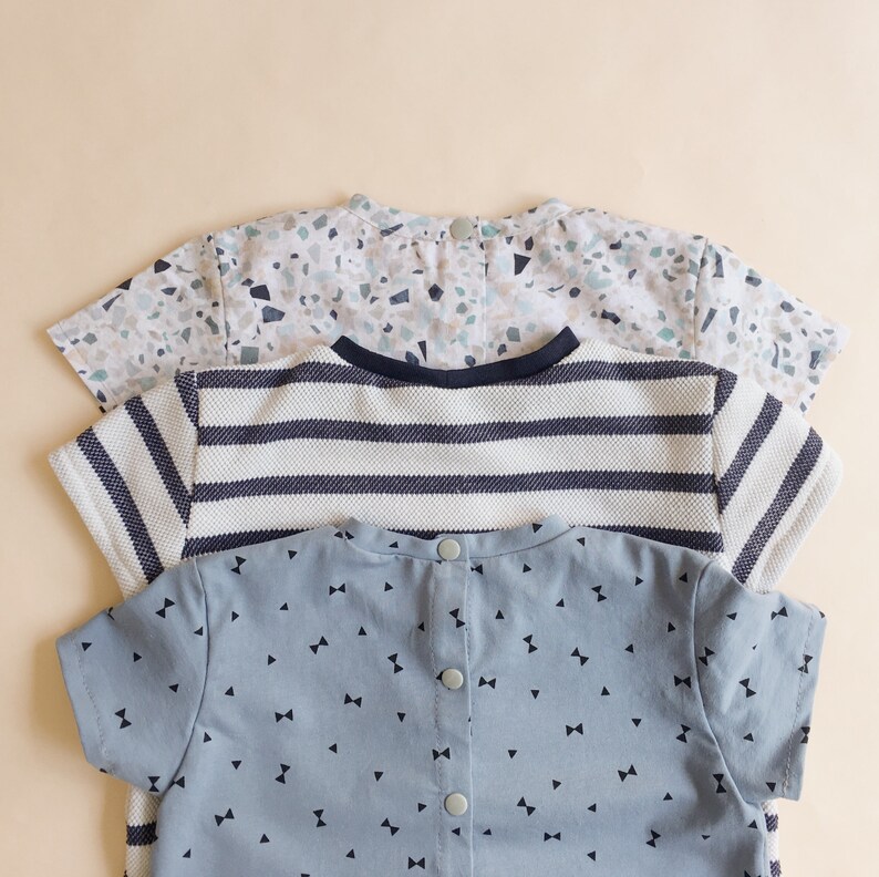K&ouml;nnte beinhalten: Drei Babyhemden mit Knopfverschl&uuml;ssen. Das oberste Hemd hat ein gesprenkeltes Muster in Blau-, Gr&uuml;n- und Beiget&ouml;nen. Das mittlere Hemd hat marineblaue und wei&szlig;e horizontale Streifen. Das untere Hemd ist hellblau mit kleinen schwarzen Fliegenmuster.