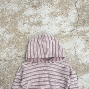 Op de afbeelding: Een gestreept hooded sweatshirt in roze en witte tinten. De trui is gemaakt van een zachte, gebreide stof.