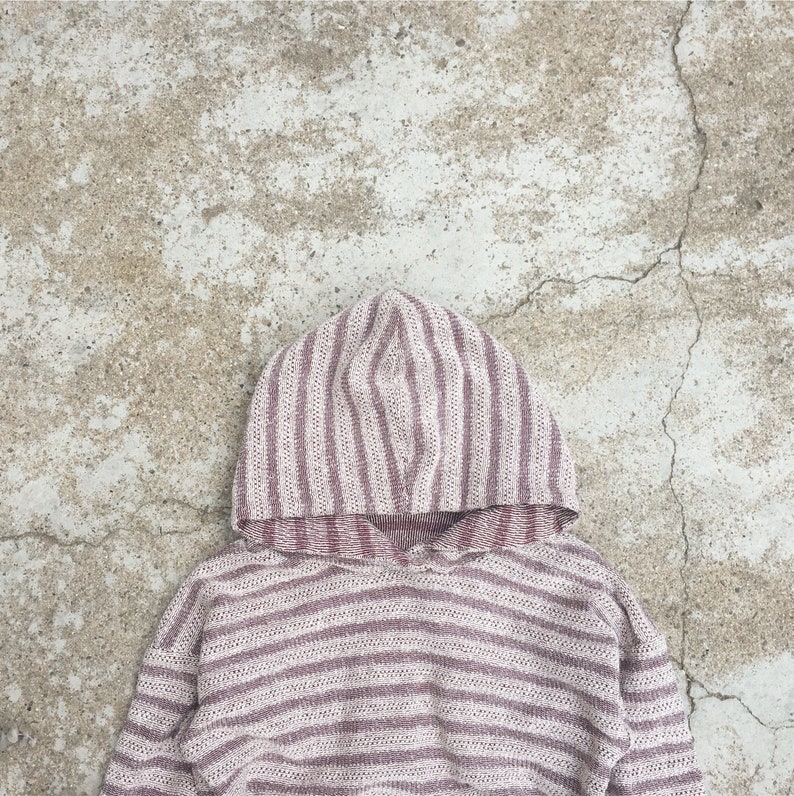 Op de afbeelding: Een gestreept hooded sweatshirt in roze en witte tinten. De trui is gemaakt van een zachte, gebreide stof.