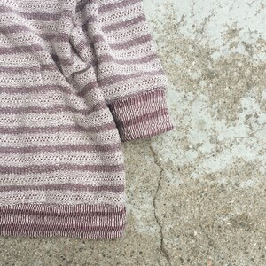 May include: A striped sweater with a white and burgundy color scheme. The sweater is made of a soft, textured fabric.