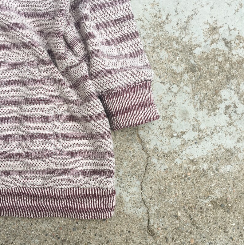 May include: A striped sweater with a white and burgundy color scheme. The sweater is made of a soft, textured fabric.