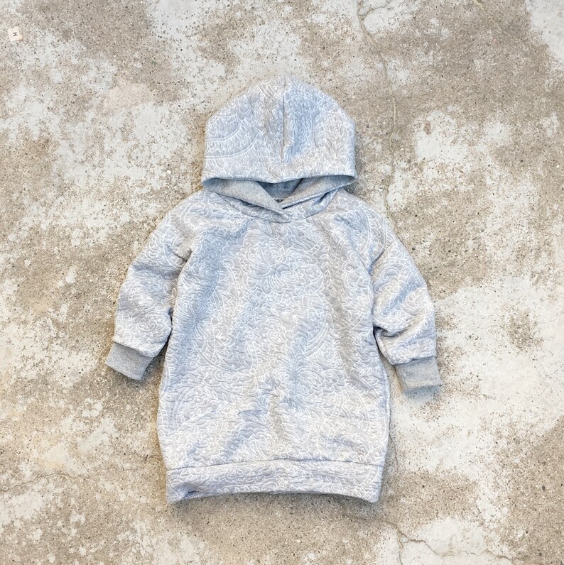 Op de afbeelding: Een grijs hoodie met een wit bloemenpatroon. De hoodie heeft lange mouwen en een capuchon met trekkoord.