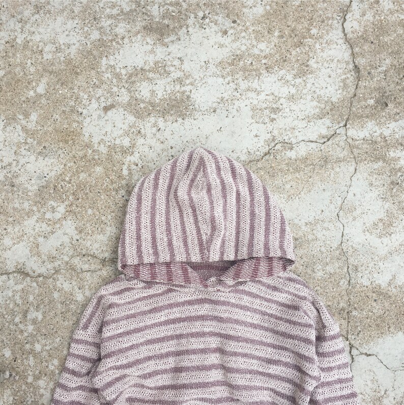 May include: A striped hooded sweatshirt in shades of pink and white. The sweatshirt is made of a soft, knitted fabric.