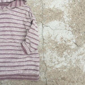 May include: A striped hooded sweater in shades of beige and burgundy. The sweater has a relaxed fit and a long sleeve.
