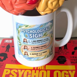 Puede incluir: Una taza de cerámica blanca con una ilustración colorida titulada Psychological Sigh con tres pasos instructivos: 1. Big inhale, 2. Slowly exhale y 3. Repeat 1-3 times. El diseño incluye pequeños dibujos de una persona demostrando la técnica de respiración.