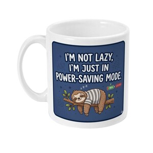 Könnte beinhalten: Ein weißer Keramikbecher mit einer blauen rechteckigen Grafik, die ein Faultier in einem grau-weiß gestreiften T-Shirt zeigt, das auf einem Ast schläft. Der Text lautet, I'M NOT LAZY, I'M JUST IN POWER-SAVING MODE, mit einem 10%-Batteriesymbol.