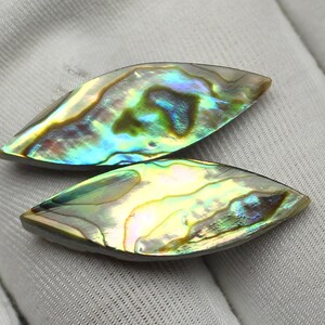 May include: Two iridescent abalone shell cabochons. The shells display a vibrant array of colors, including blues, greens, yellows, and hints of purple. The cabochons have a smooth, polished surface and a teardrop shape, perfect for jewelry making.