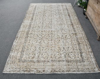 Puede incluir: Una alfombra vintage de color crema con un patrón floral marrón. La alfombra tiene un aspecto desgastado y un borde con flecos.