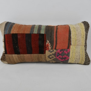 Puede incluir: Una almohada rectangular de patchwork con una variedad de colores y patrones, incluyendo rojo, naranja, marrón, beige y azul. La almohada está hecha de tejido tejido y tiene una superficie ligeramente texturizada.