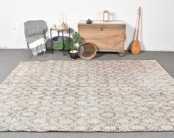 Puede incluir: Una alfombra grande y estampada en tonos beige, gris y blanco. La alfombra tiene un diseño floral y está colocada sobre un suelo gris.