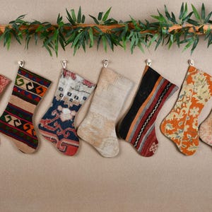 May include: Eight colorful Christmas stockings with intricate patterns and designs. The stockings are made from a variety of fabrics and are hung on a wall.