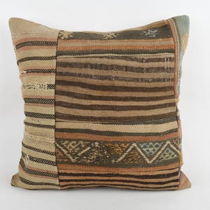 May include: Square decorative pillow with a patchwork design. The pillow features a mix of tan, brown, and orange hues with striped and geometric patterns. The pillow is made of a woven fabric.