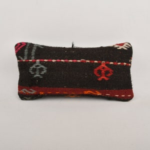 May include: A small, rectangular pillow with a black background and colorful geometric patterns. The pillow is made of woven fabric and has a fringed edge.