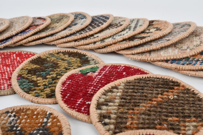 May include: A set of colorful round coasters made from woven fabric with a beige trim. The coasters feature various patterns and colors, including red, green, brown, and beige.