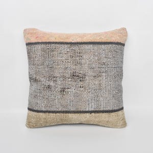 Può includere: Cuscino decorativo quadrato con una trama tessuta. Il cuscino presenta un centro grigio chiaro con una striscia grigio scuro e un fondo beige. Il bordo superiore è di colore pesca chiaro. Il cuscino viene probabilmente utilizzato per l'arredamento della casa.