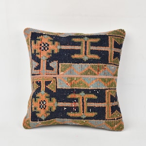 May include: A square throw pillow with a geometric pattern in shades of blue, green, orange, and brown. The pillow has a dark blue background with a repeating pattern of orange and green geometric shapes.