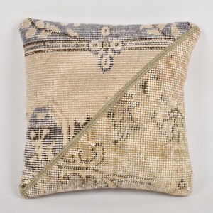 May include: Square cushion with a patchwork design. The cushion has a beige and tan background with a geometric pattern and a diagonal seam. The top edge has a blue and black border.